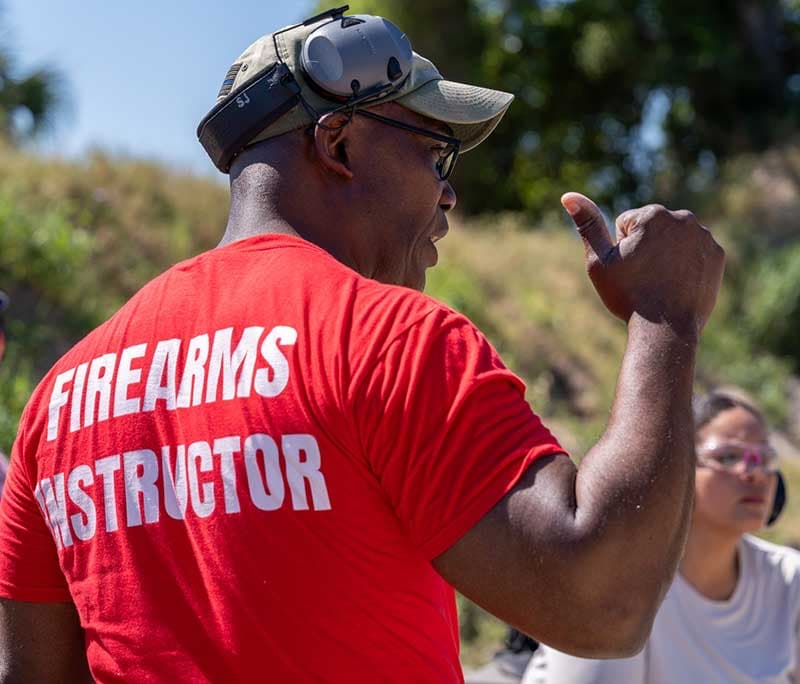 Sanfa Johnson coaching a student on the range, wearing a firearms instructor shirt